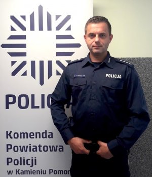asp. szt. Tomasz Cesarski na tle banneru Komendy Powiatowej Policji w Kamieniu Pomorskim